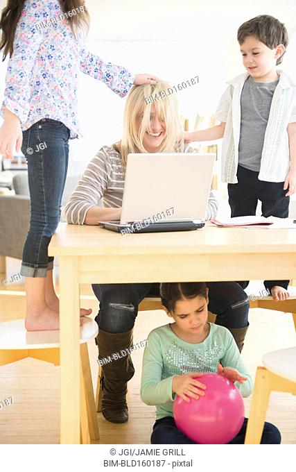 Caucasian mother using laptop with chaotic children