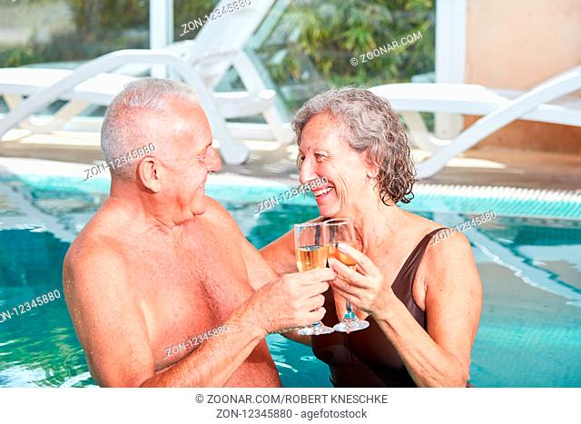 Senioren Paar feiert mit einem Glas Sekt im Schwimmbad im Wellnesshotel