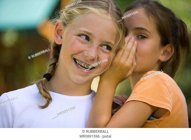 Close-up of a girl whispering into her friends ear