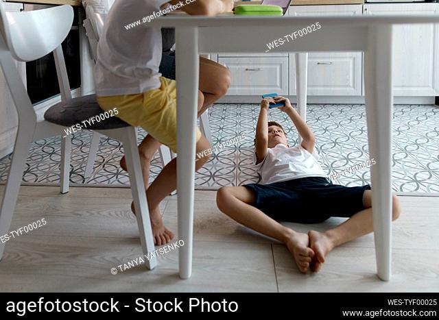 Boy using mobile phone under table lying on floor