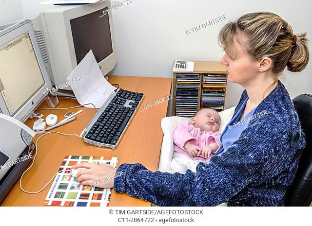 mother working at computer holding newborn baby