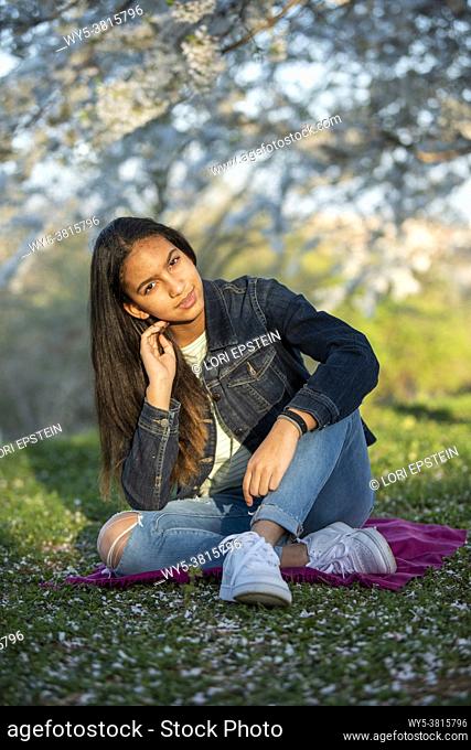 Outdoor portrait of mixed race teenage girl in a grove of cherry trees at sunset in the springtime