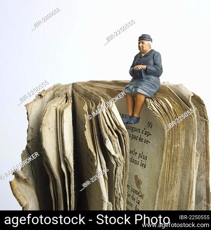 Elderly lady, miniature figurine, sitting on an old book