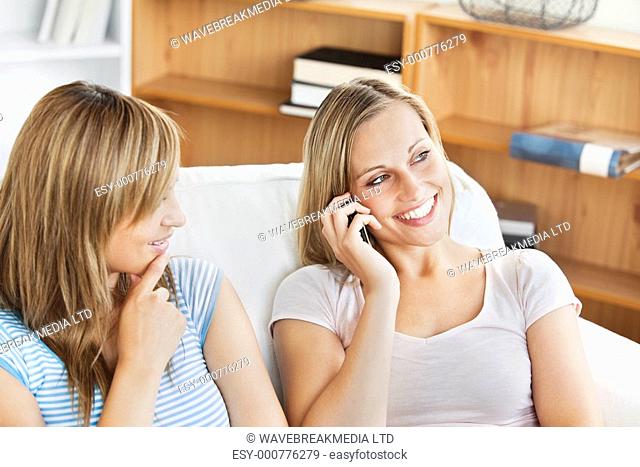 Two pretty women using a cellphone at home in the living-room