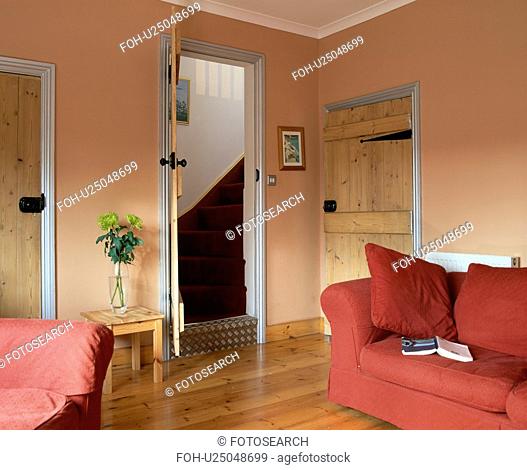 Red sofa and wooden flooring in economy-style living room with view of stairs through open door