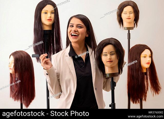 A YOUNG HAIRSTYLIST CHEERFULLY POSING WITH DUMMY HAIR