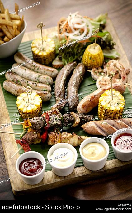 organic mixed grill barbecue meat platter rustic set meal with sausages, skewers, side dishes and sauces