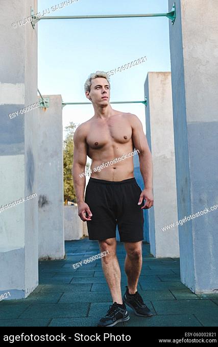 Natural portrait of young athletic shirtless man standing near concrete wall