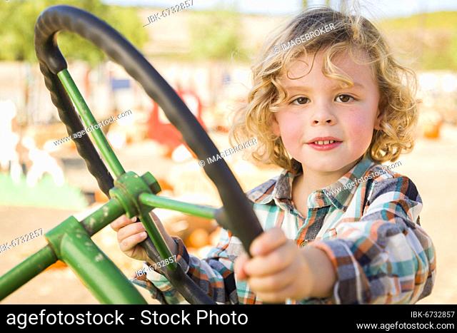 Adorable young boy playing on an old tractor in a rustic outdoor fall setting