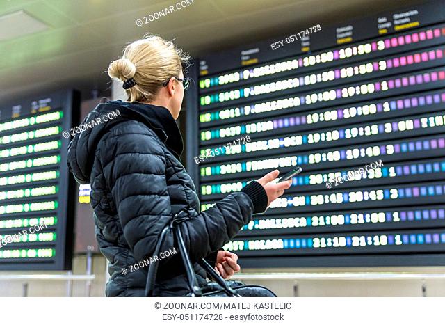Casual woman in international airport looking at the flight information board, checking her flight