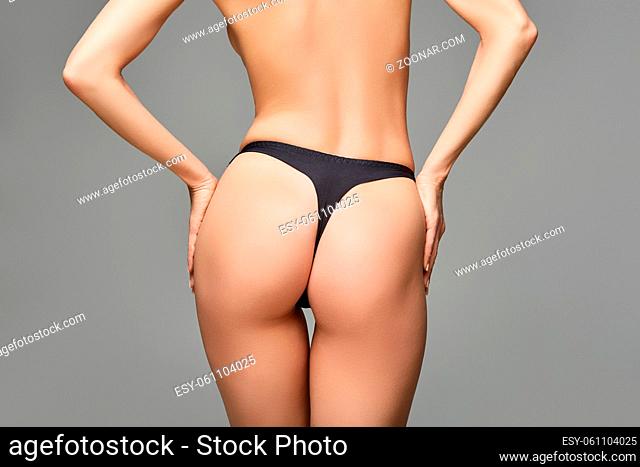 beautiful young woman fit butt on in black panties. studio shot on grey background. copy space