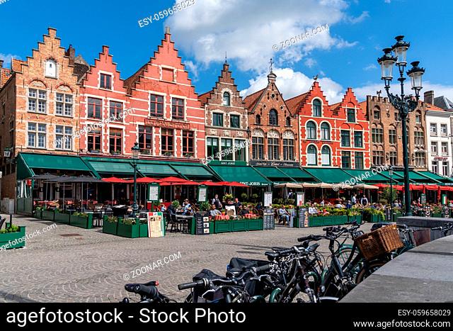Bruges, Belgium - 12 May, 2021: people enjoy a day out in the restaurants on Market Square in Bruges with many historic brick buildings in the background