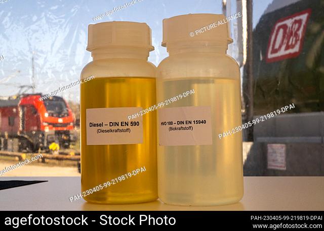 05 April 2023, Bavaria, Munich: A bottle of normal diesel (l) and a bottle of HVO fuel are on display on a table against the backdrop of a refueling facility...