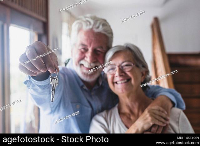 Happy senior old aged woman and man customer landlord hold key to new house apartment give to camera, older retired couple of seniors hand real estate owner...