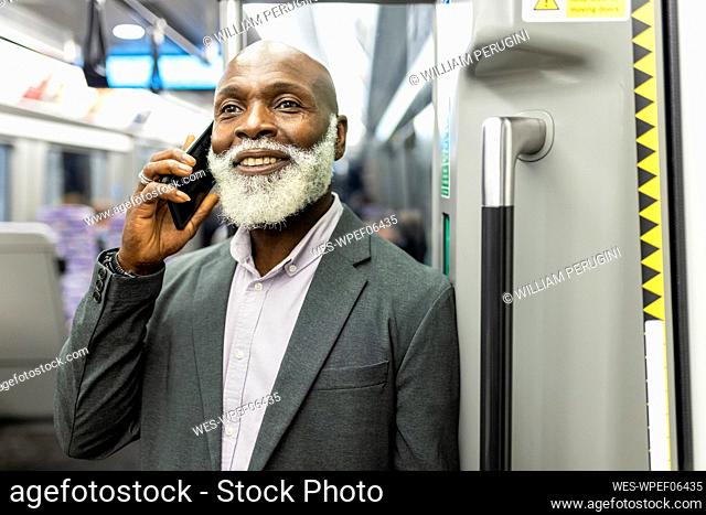 Smiling businessman talking on smart phone in train