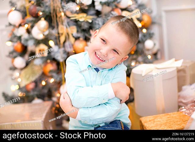 Joyful cheerful child at the New Year tree. The boy smiles on the background of the Christmas interior