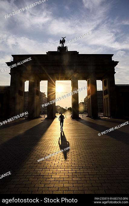 19 August 2023, Berlin: A man walks through the Brandenburg Gate as the sun rises. People in Berlin and Brandenburg have to prepare for strong to extreme heat...