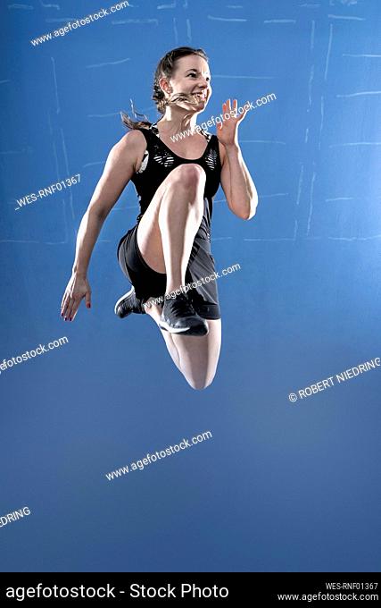 Young woman jumping high in front of blue wall