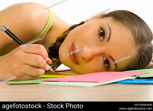 Young, beautiful woman lying on desk. Smiling and writing a letter. Looking at camera. White background