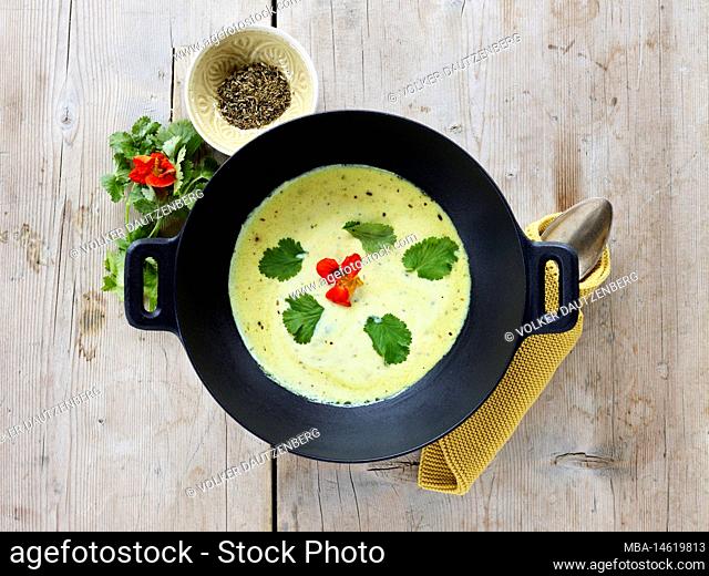 ayurvedic cuisine, buttermilk soup in a black cast iron cooking pot from above, next to a small bowl with cumin, on light rustic wooden table top