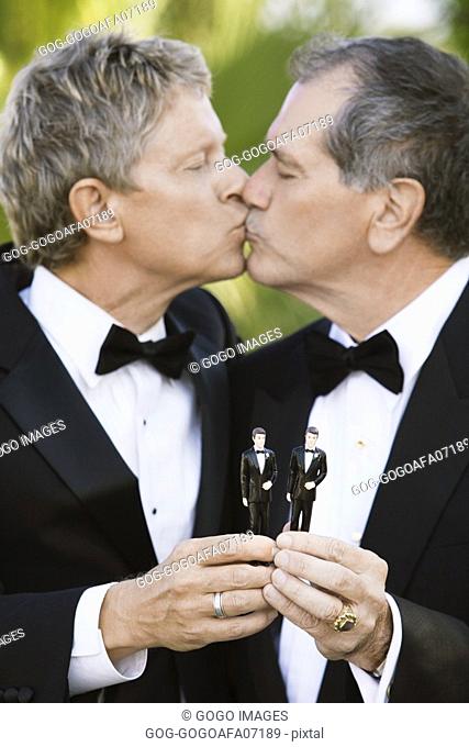 Newlywed gay couple kissing while holding two plastic grooms