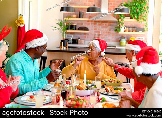 Diverse group of happy senior friends in holiday hats celebrating christmas together at home