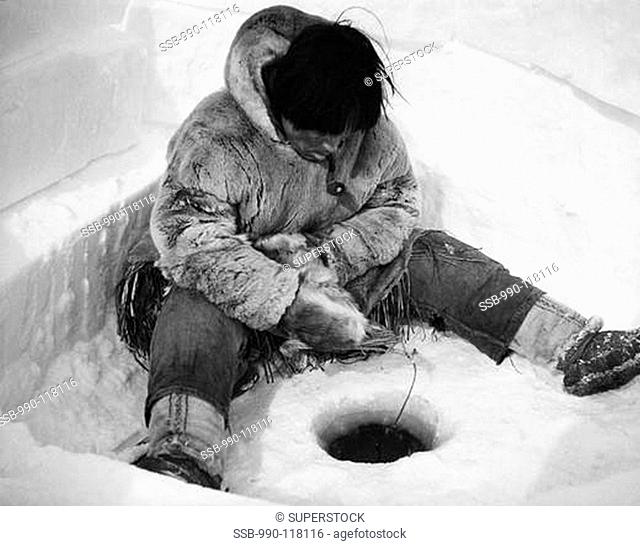 Eskimo fisherman sitting near a hole and fishing, Alaska, USA