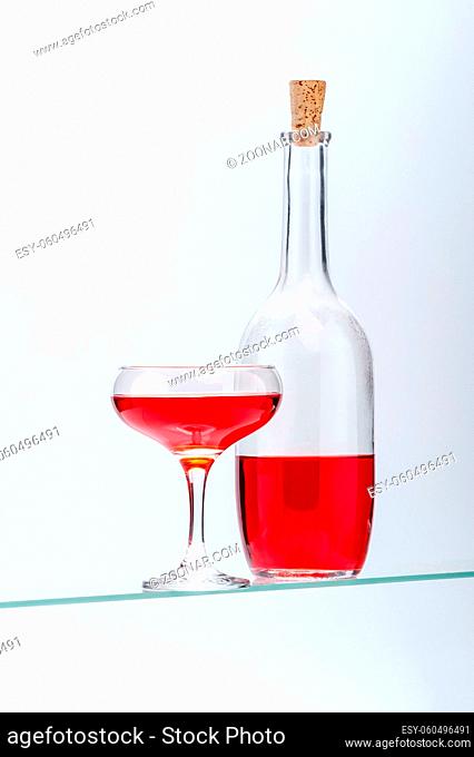Wine glass and bottle with red alcoholic drink on a light gray background