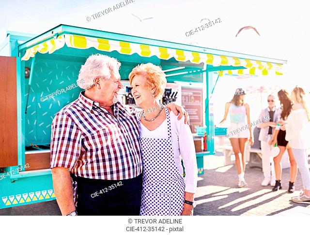 Smiling affectionate senior couple business owners outside sunny food cart