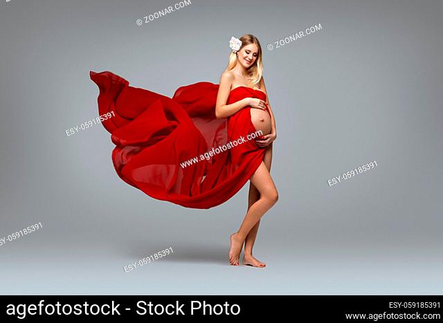 Beautiful young pregnant woman in red dress on grey background. Copy space