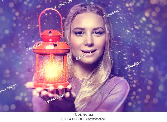 Portrait of a beautiful woman holding on hand red retro style glowing lantern over night starry sky background, magical Christmas fairytale