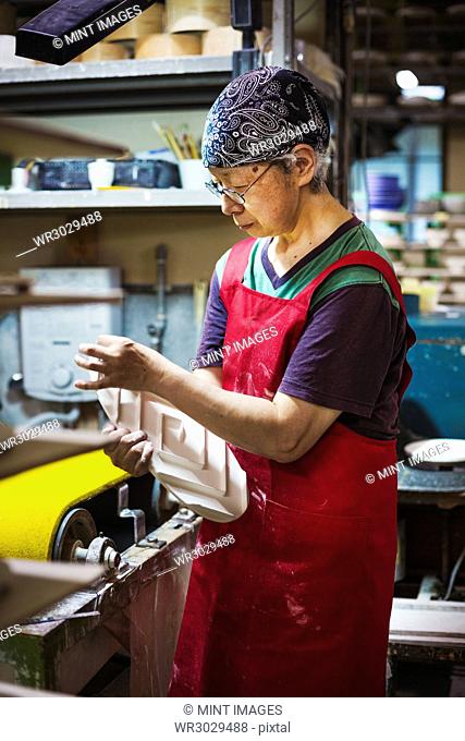 Woman working in a Japanese porcelain workshop, wearing apron, holding white porcelain object