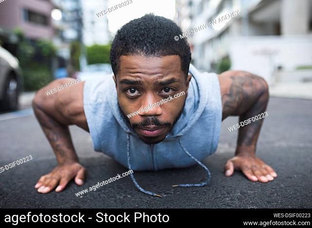 Young sportsman doing push-ups with determination on street