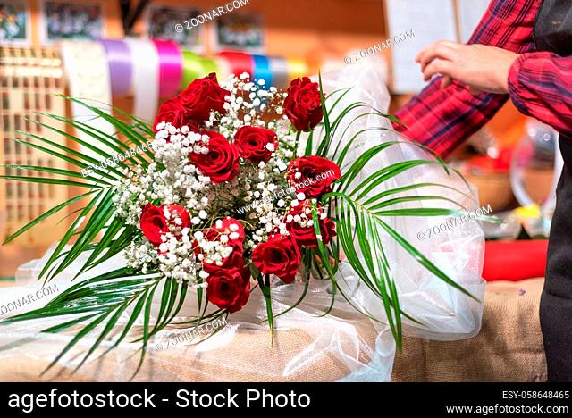 Young woman owner of florist shop arranging bouquet of roses
