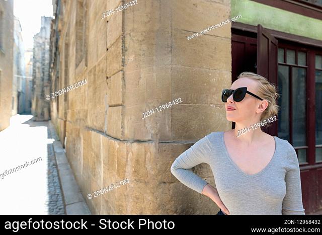 Portrait of a beautiful blonde woman with sunglassess exploring the medieval city. Tourist in France