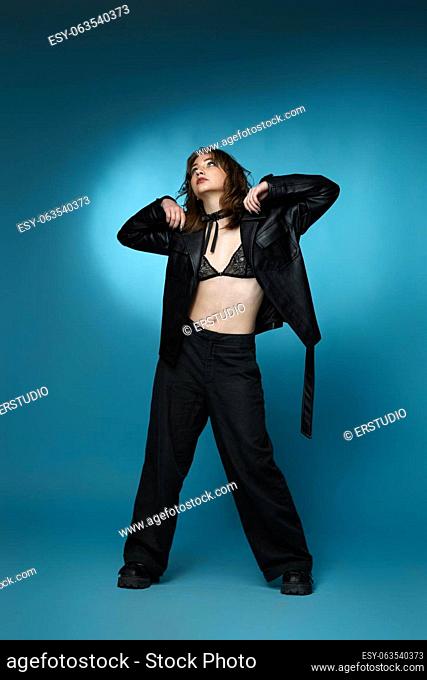 young stylish woman posing in black leather jacket and pants on blue background