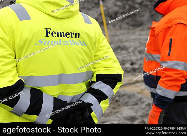 17 March 2022, Schleswig-Holstein, Fehmarn: The words ""Femern Sund Baelt"" are printed on the jacket of a man standing on the construction site of the Baltic...