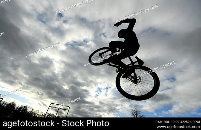 10 January 2020, Hessen, Frankfurt/Main: A teenager jumps with his dirtjump bike on the skater area in the Osthafenpark in front of a cloudy sky