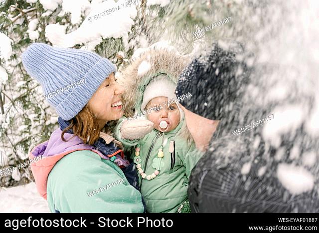 Woman carrying daughter by man playing with snow in winter
