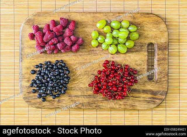 Fresh berries: raspberries, gooseberries, currants, red currant on an oak cutting board. Flat lay, top view