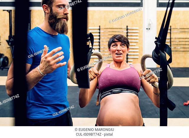 Trainer guiding pregnant woman using exercise equipment in gym