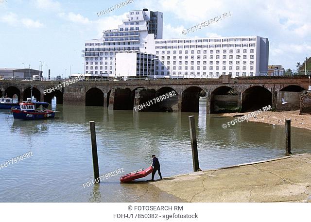 Man launching a rubber boat in the harbour at Folkestone in Kent with railway bridge & large white building in background