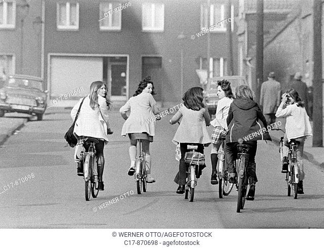 Seventies, black and white photo, people, six young girls on bicycles drive side by on a traffic road, pleasure trip, excursion, aged 13 to 16 years