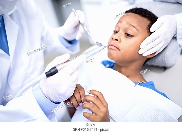 MODEL RELEASED. Scared boy looking at dental drill in dentist's hand