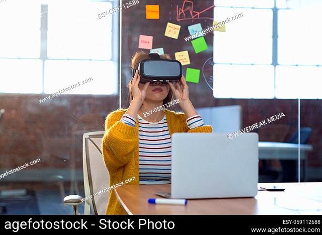Portrait of asian businesswoman sitting in front of laptop wearing virtual reality headset