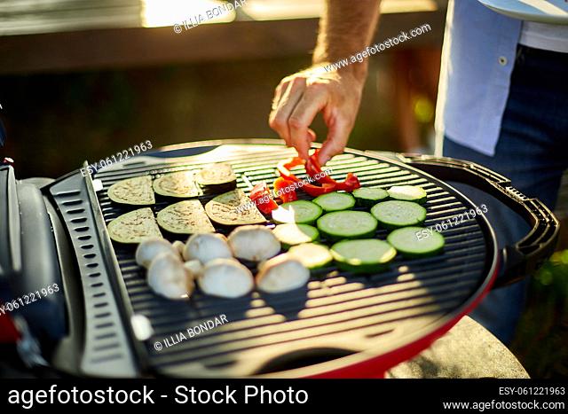 Close up on man's hand roasting vegetables on the barbecue gas grill outdoor in the backyard, Vegetables On Grill, summer family picnic, food on the nature