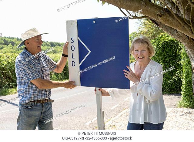 Couple standing with a sold sign outside their home