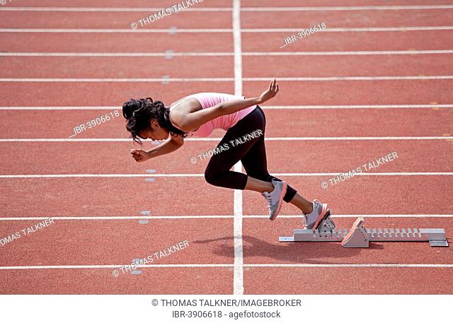 Sporty young woman starting from starting block to run on running track