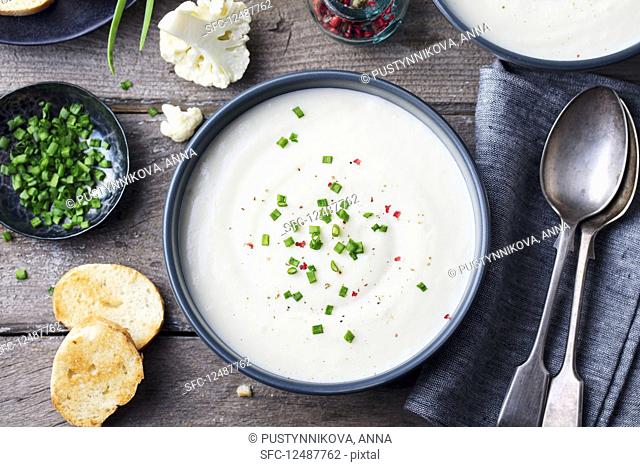 Cauliflower, potato cream soup with green onion in black bowl on grey wooden background