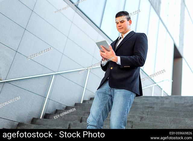 Young and Casual Businessman Using Tablet while Walking Outside of Office Building
